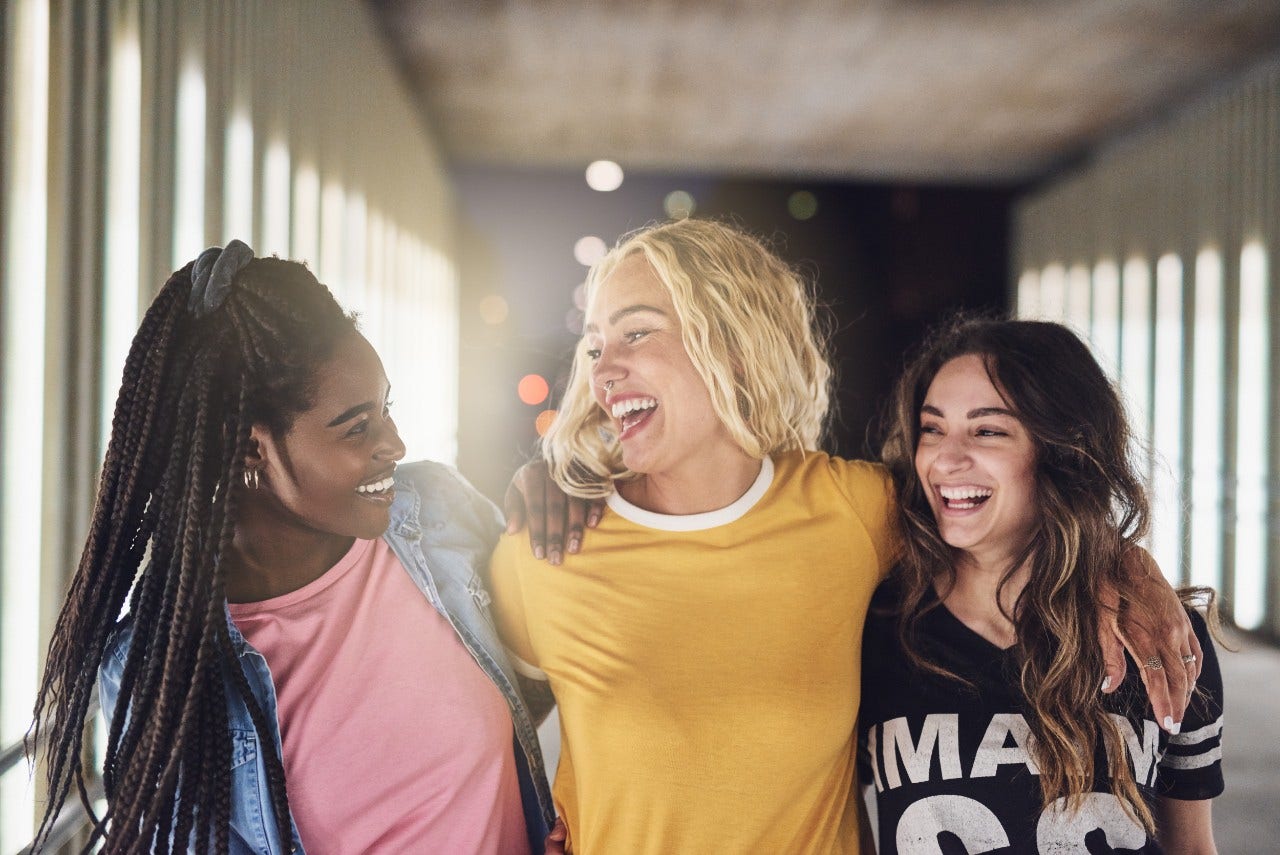 Laughing group of diverse young girlfriends having fun while walking together down a walkway in the city at night