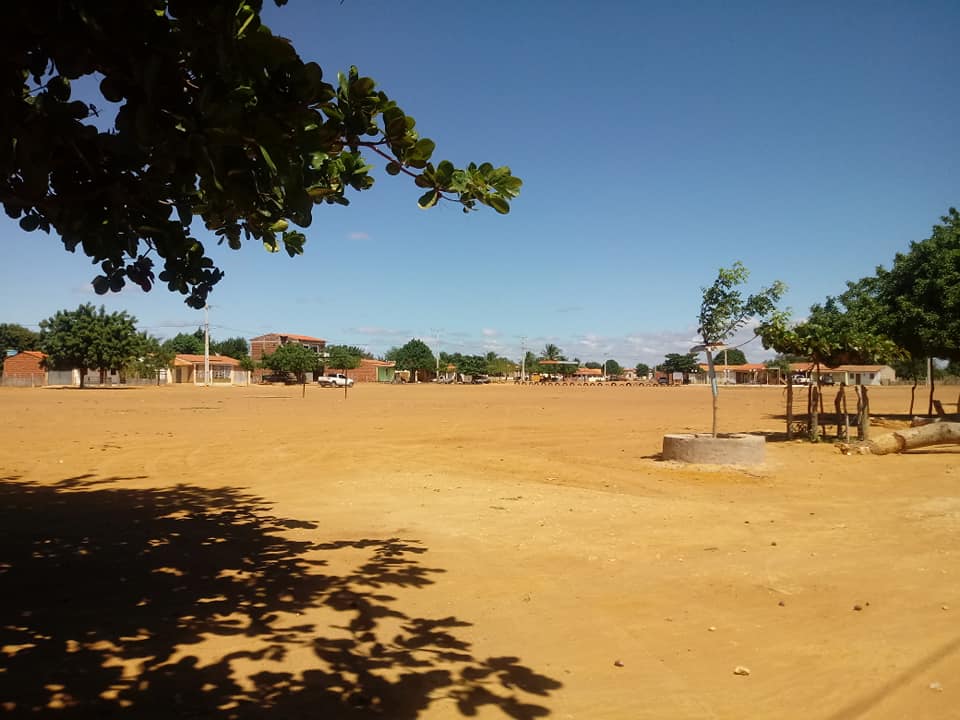 Dia ensolarado com chão de terra batida. Uma árvore faz sombra à esquerda.