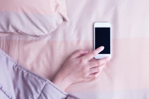 Woman hand under blanket being woken by mobile phone in bedroom.