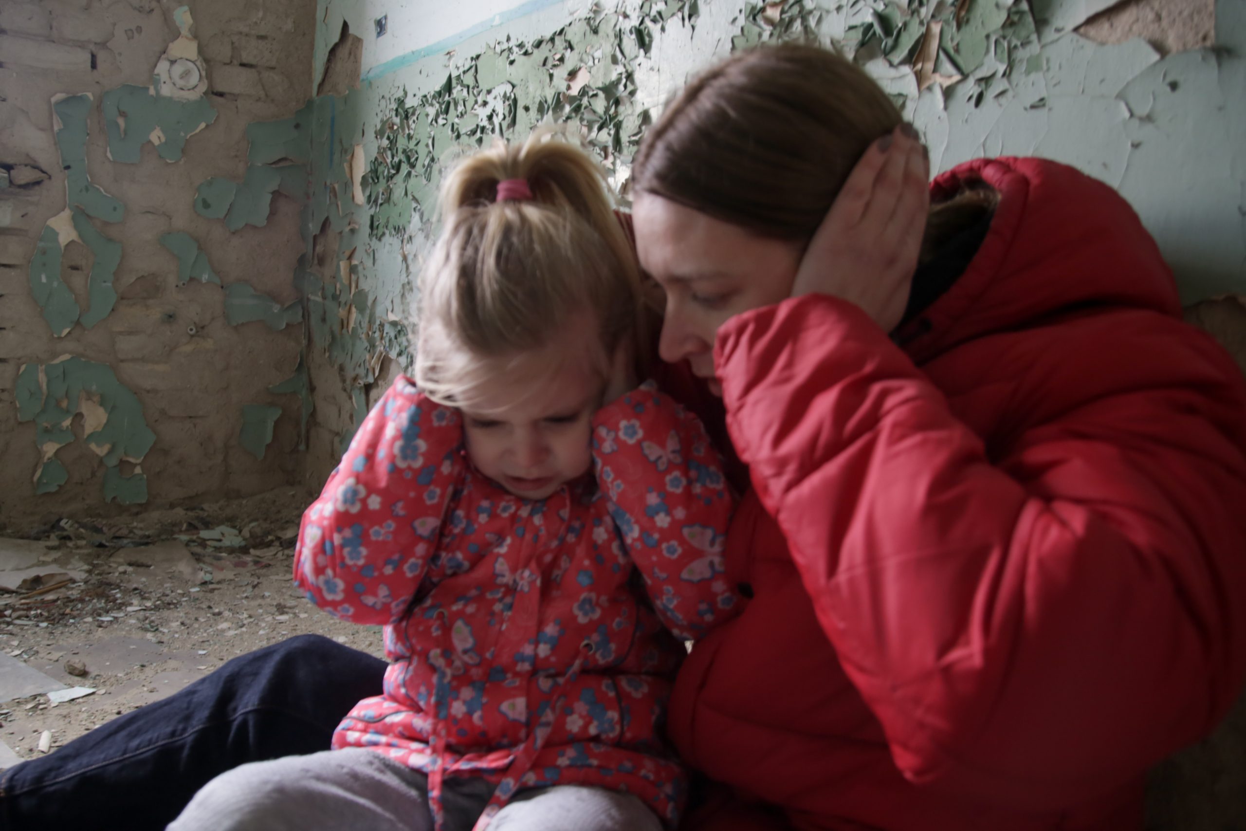 Refugee mother and daughter cover the ears in a shelter