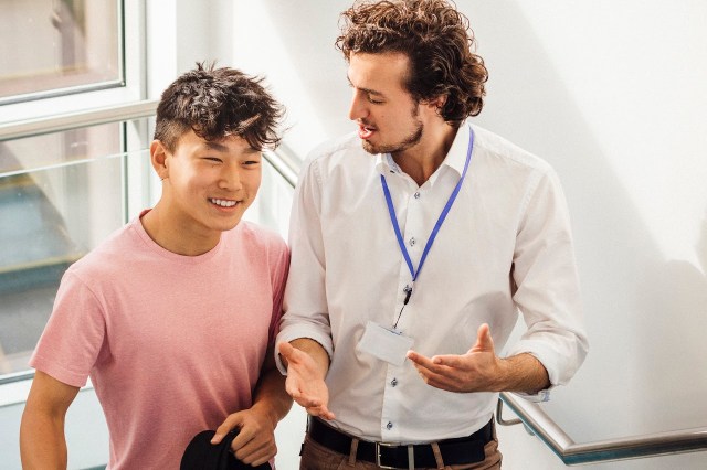 Student and his teacher make their way up the school staircase. They look happy as they talk.