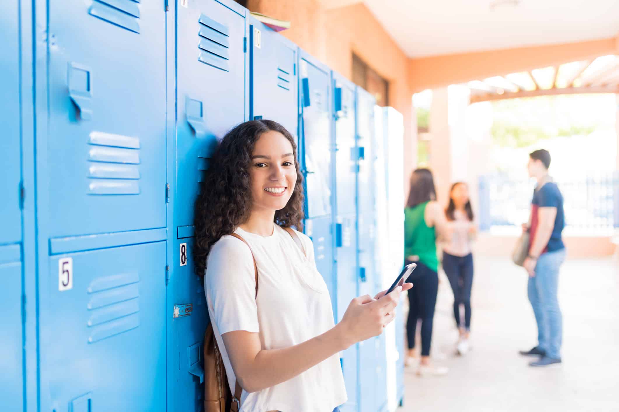 Smiling Caucasian teenager using smartphone in high school corridor