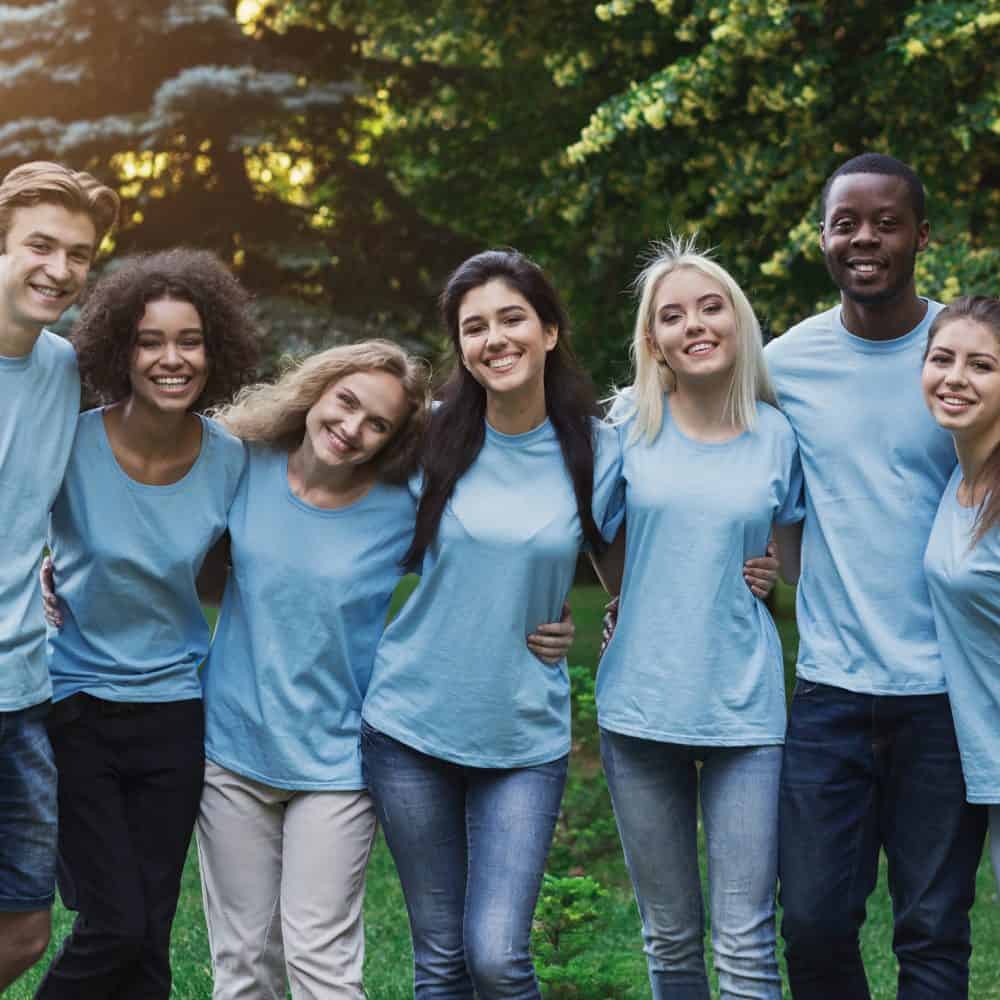 Group of happy young diverse volunteers embracing at park, ready for work, copy space