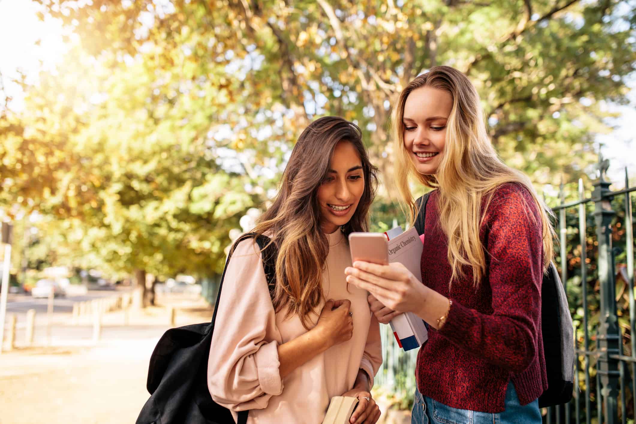 University female students reading message on smart phone outdoors. Beautiful students looking at mobile phone.