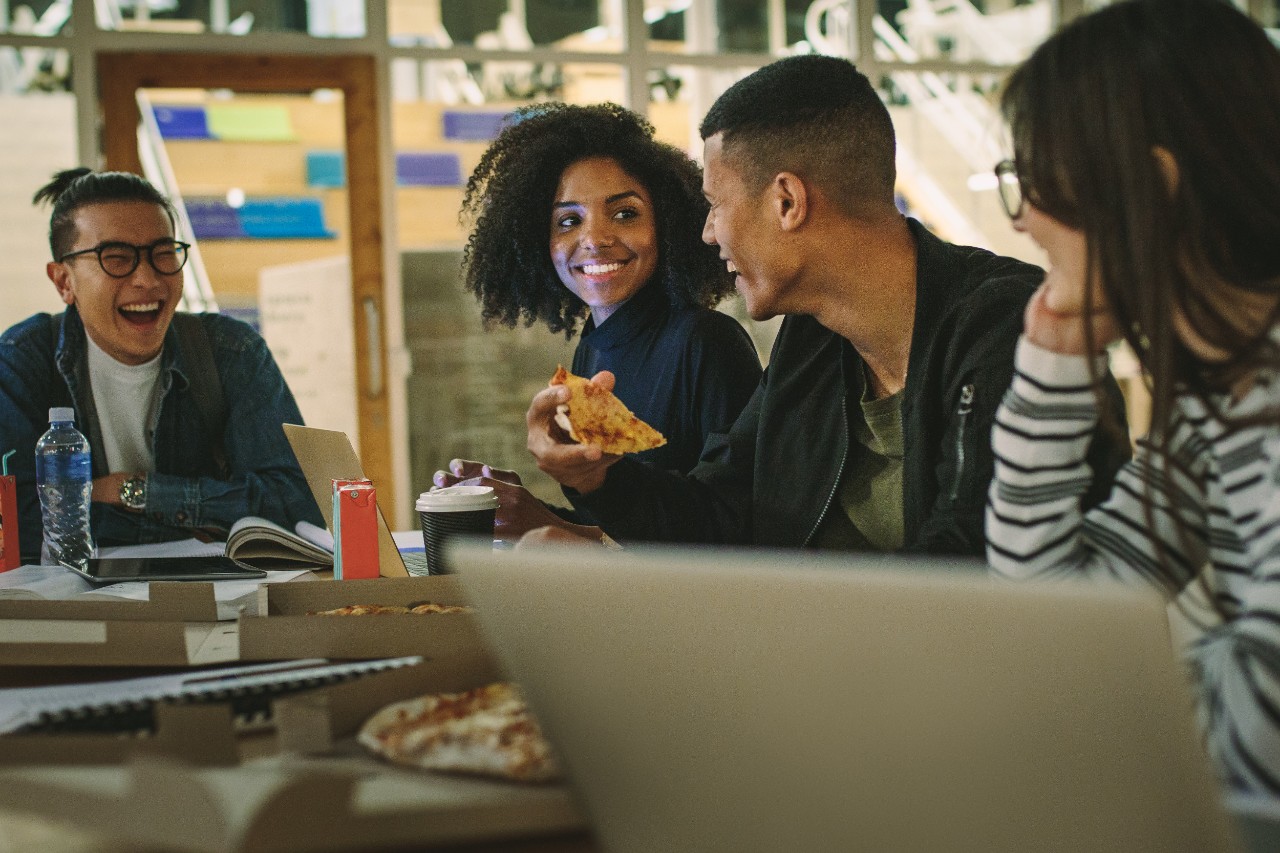 Group of students eating pizza at college canteen. Multi-ethnic men and women students eating at university campus cafe.