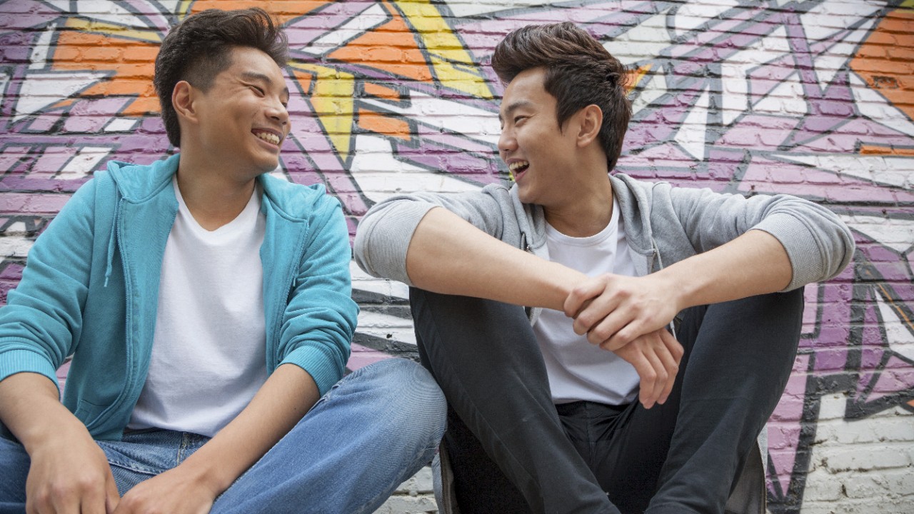 Two young men hanging out in front of graffiti wall