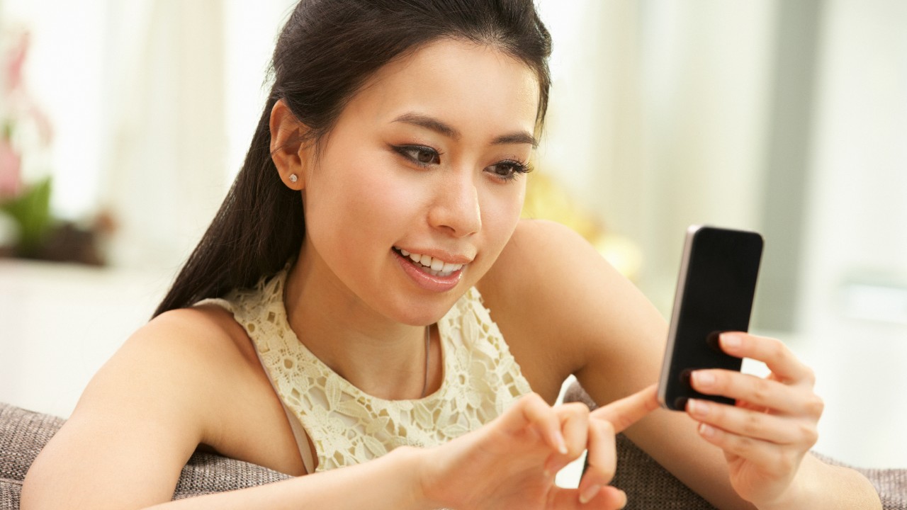 Young Chinese Woman Using Mobile Phone On Sofa At Home