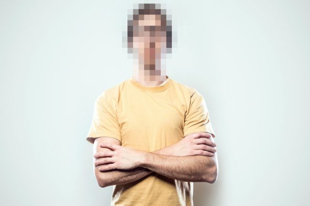 A portrait of a hipster young man from the waist up, whose face has been rendered unrecognizable by being pixelated.  A conceptual representation of individual identity protection.  Square crop with copy space on a a clean off-white background.