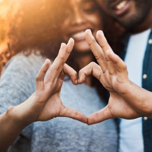 Shot of a a young couple making a heart shape with their fingers outdoors