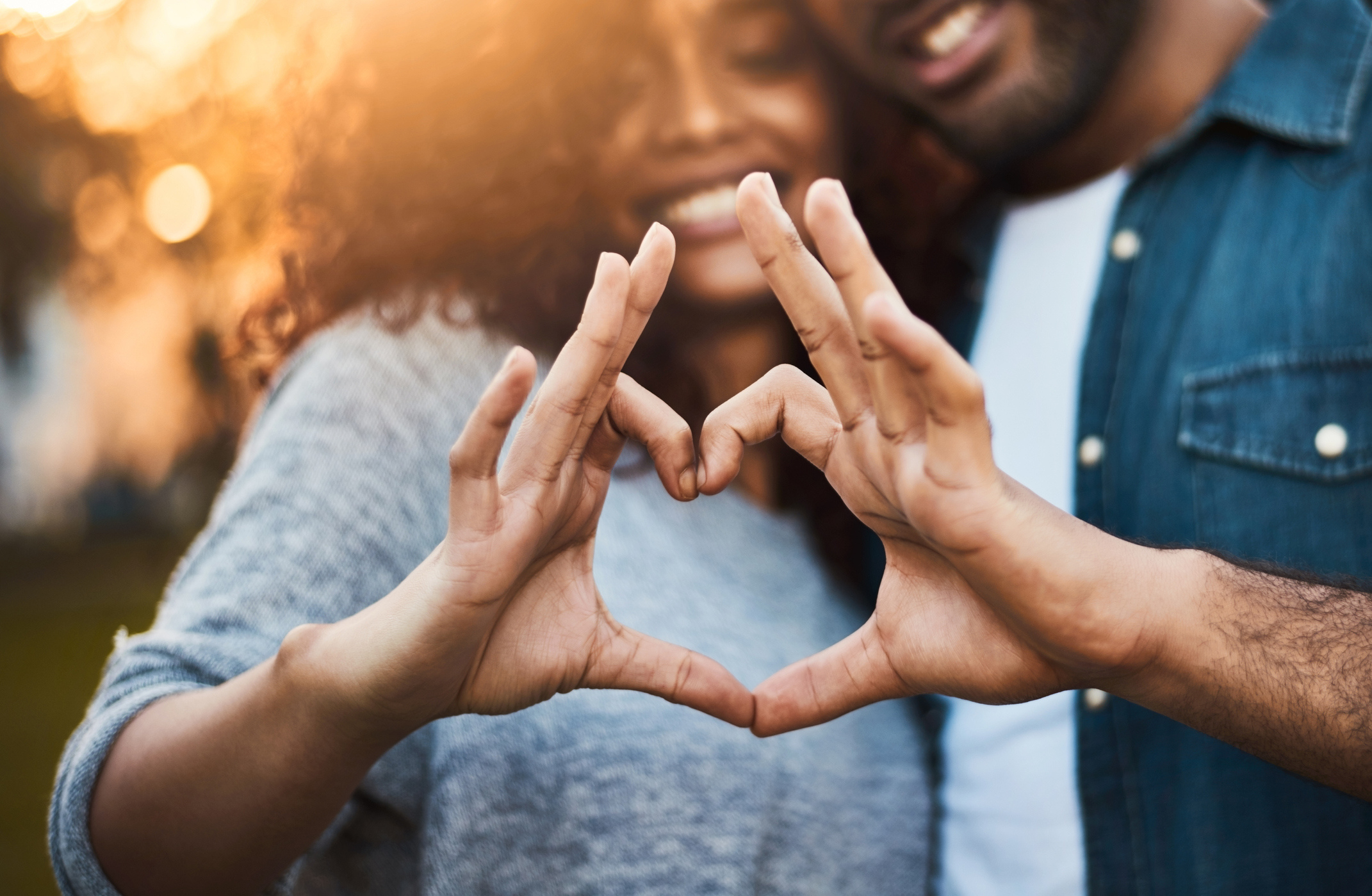 Shot of a a young couple making a heart shape with their fingers outdoors