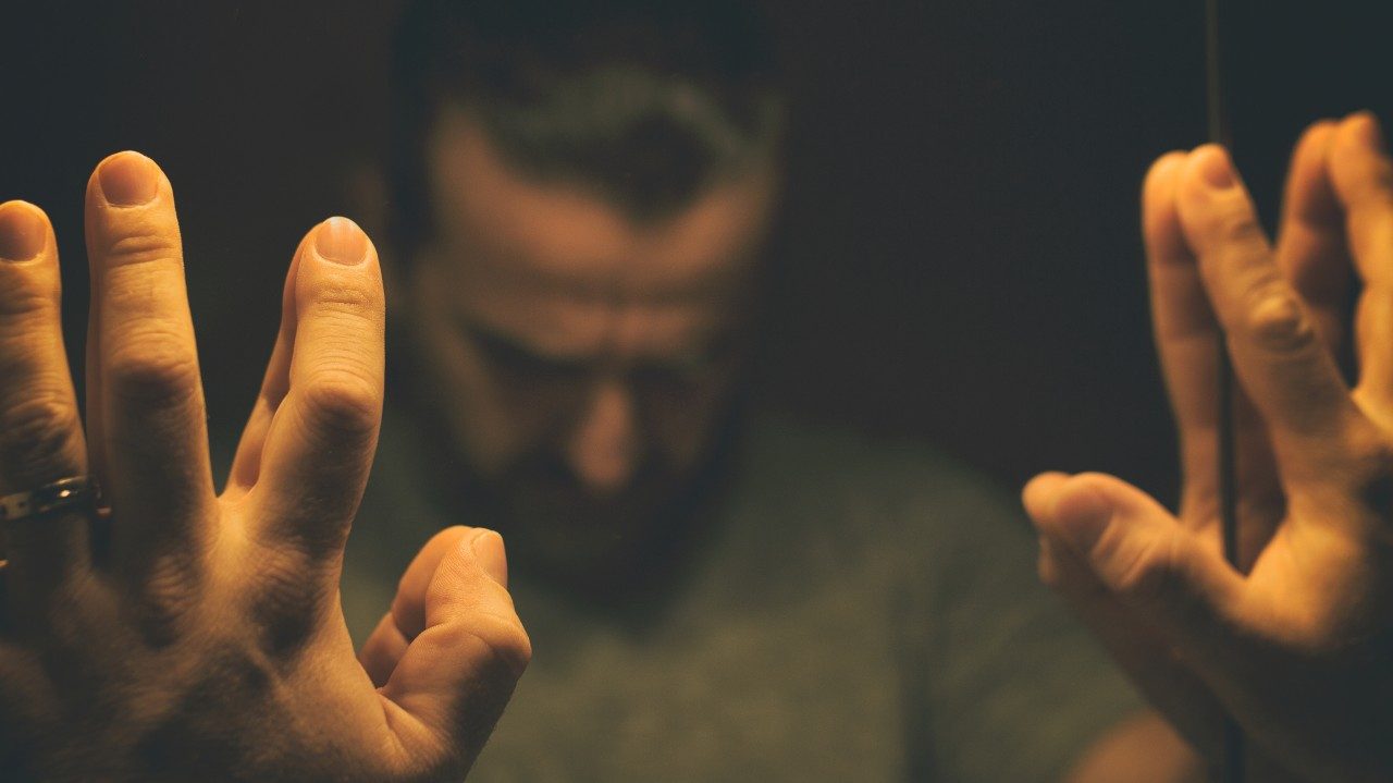 man looking down with hands against mirror