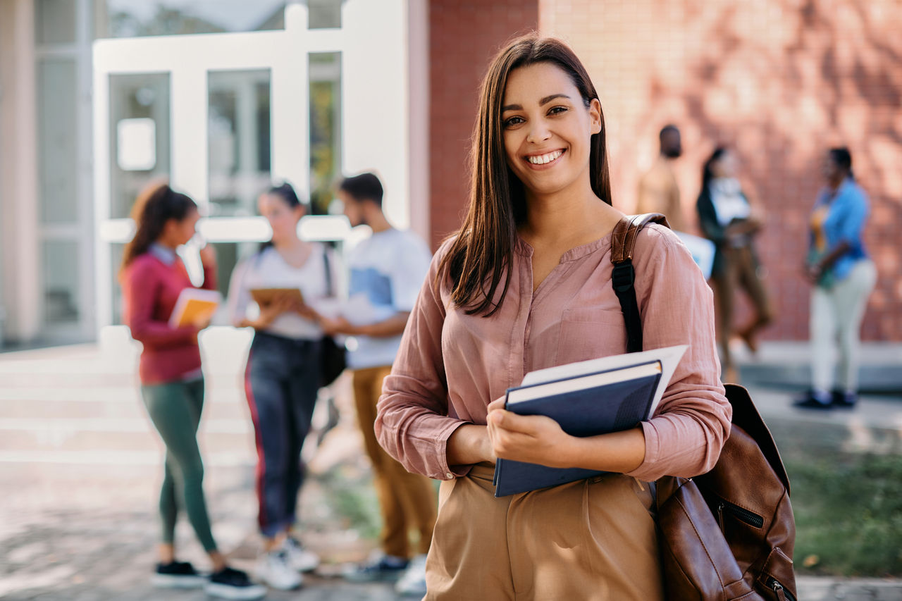 Happy university student going on a class at the university and looking at camera. 